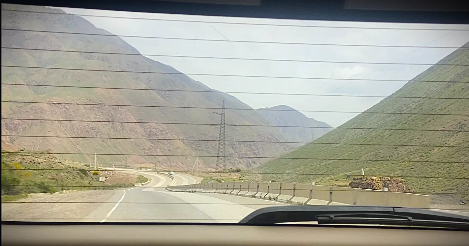 A scenic view of a winding road flanked by tall, green mountains in a rural area.