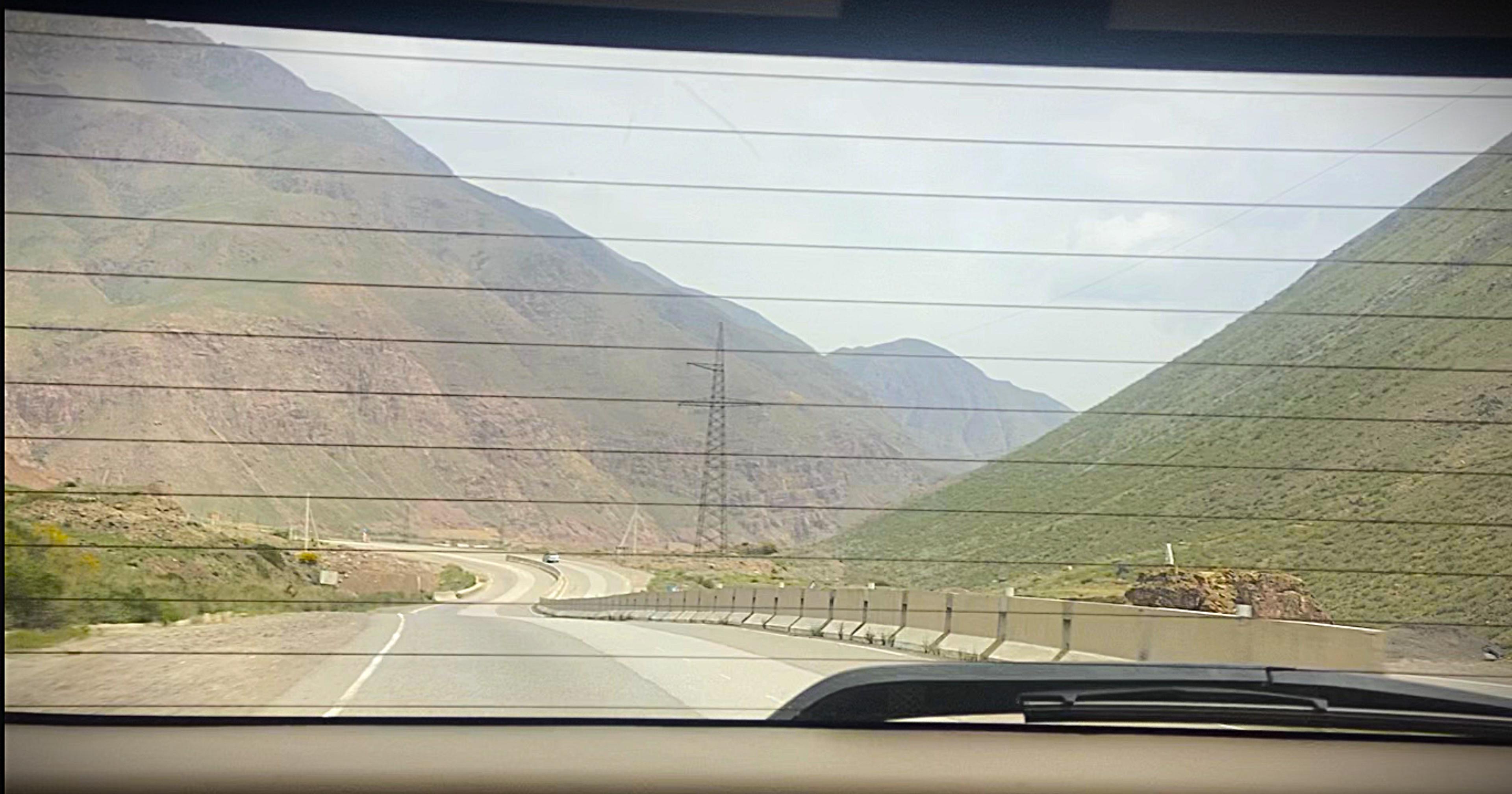 A scenic view of a winding road flanked by tall, green mountains in a rural area.