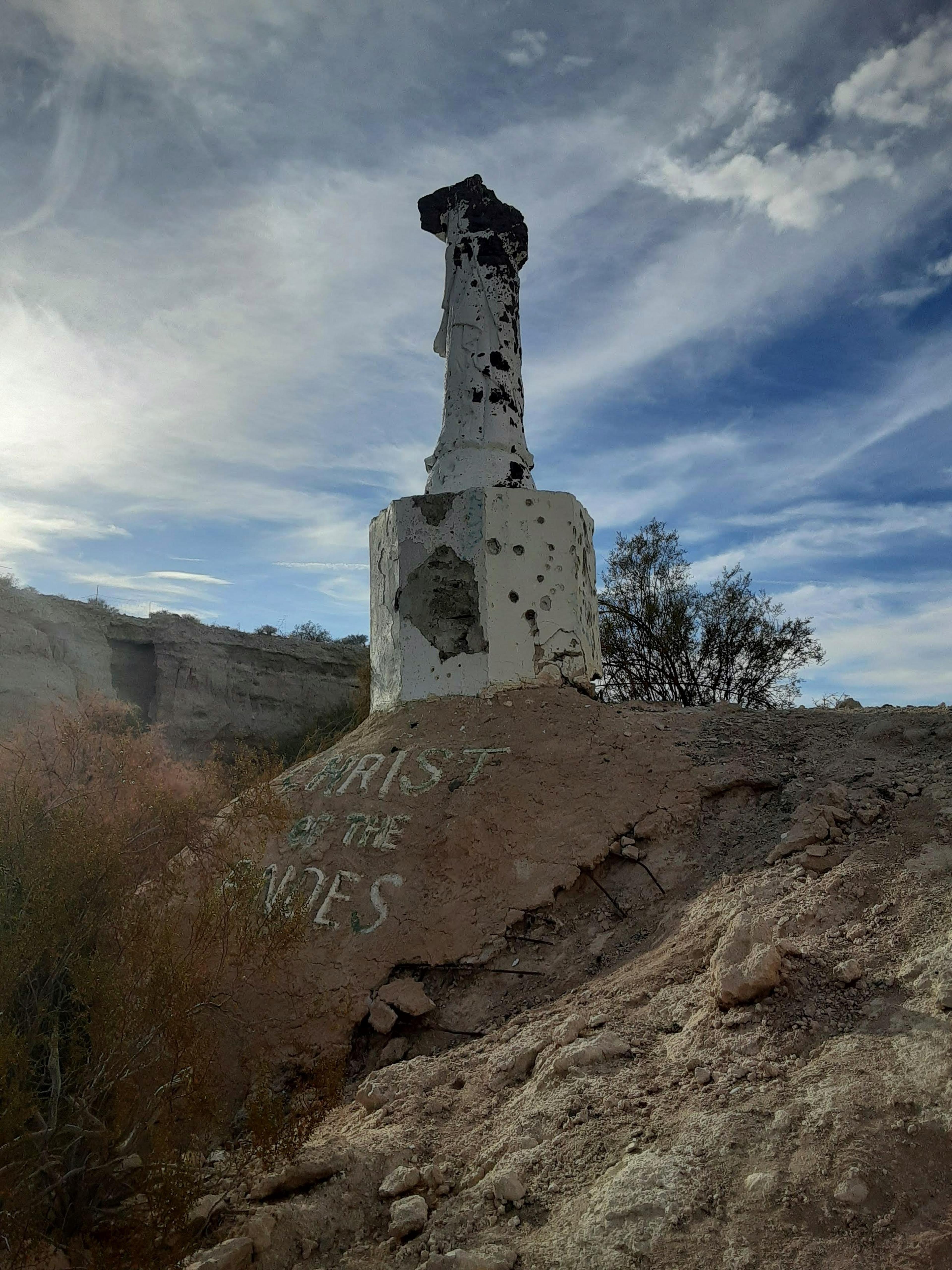 An eroded statue labeled "Christ of the Andes" stands amidst a rugged landscape at the top of a canyon.