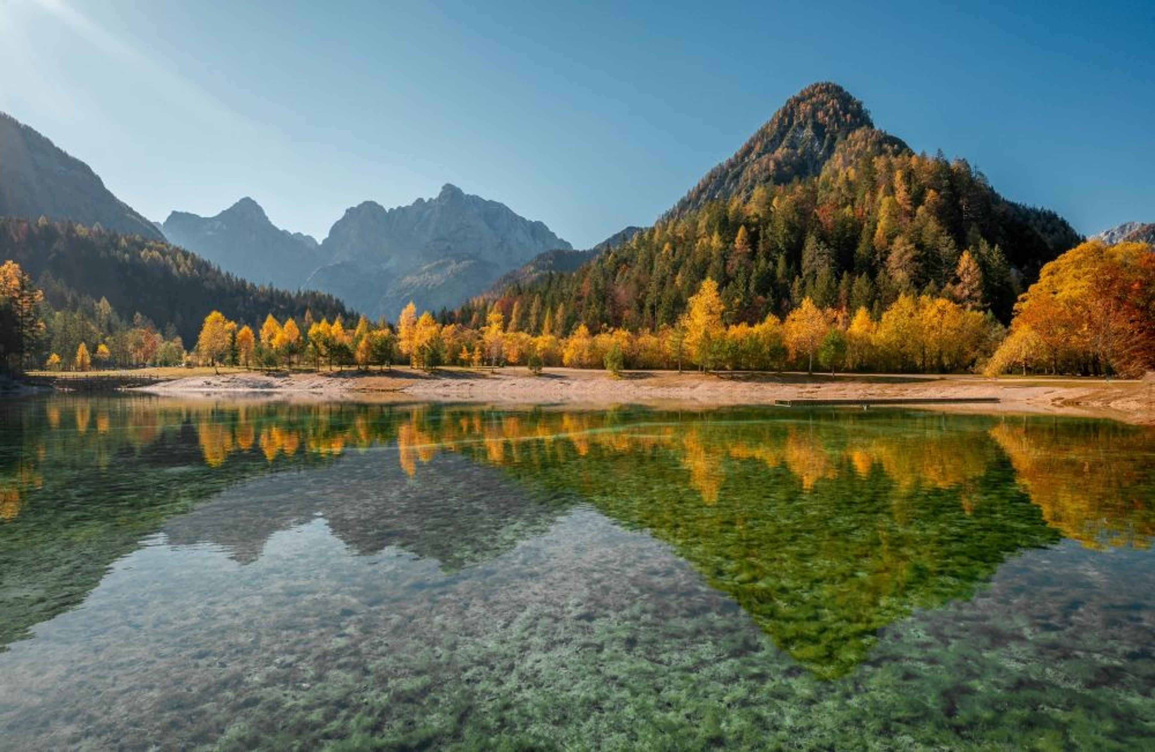 A tranquil autumn landscape reflects on the crystal-clear waters of Lake Jasna in the Julian Alps, Slovenia.