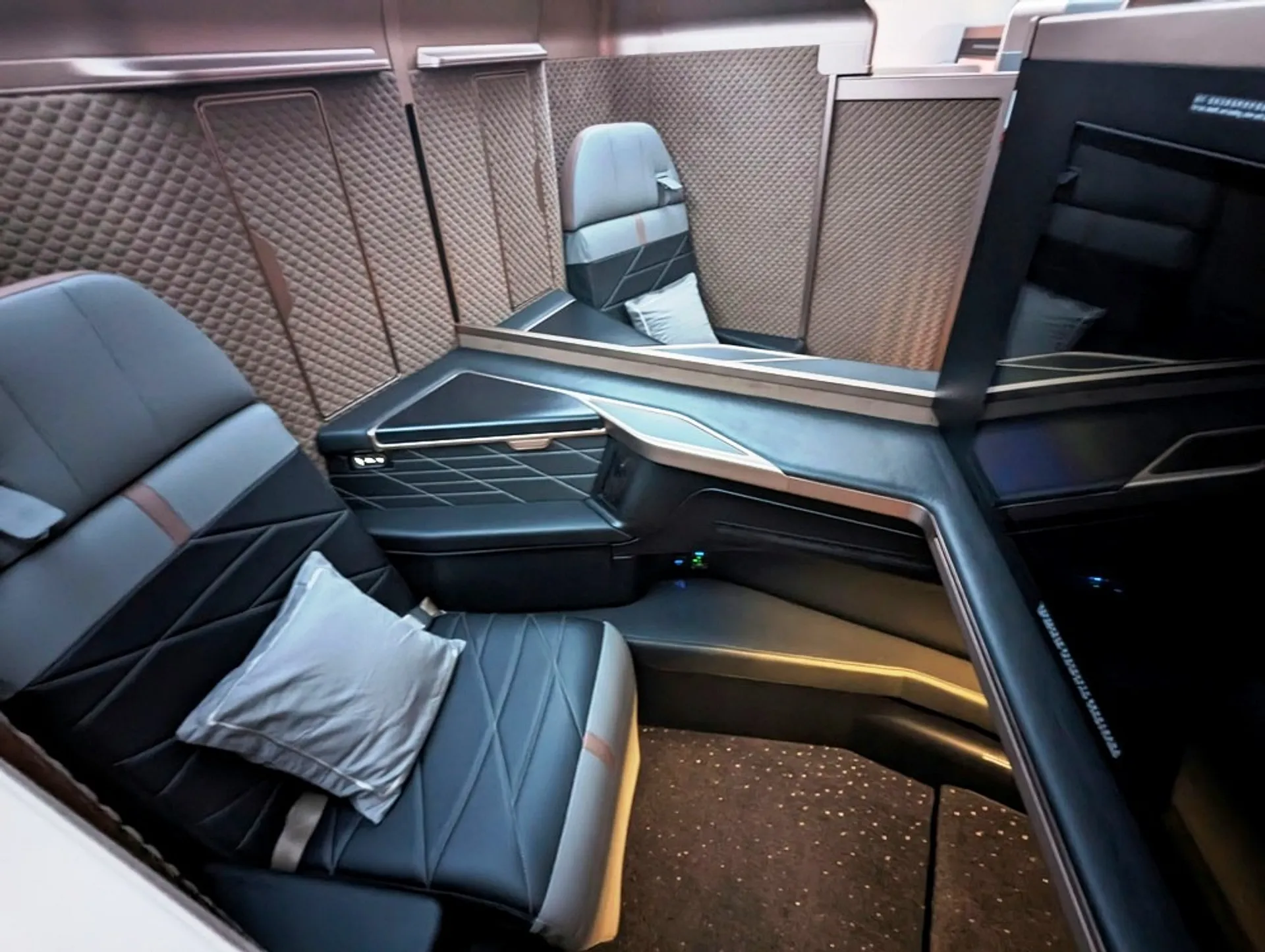 A luxurious airline first-class suite with sleek, modern design and plush seating likely from an aircraft's upper-class section.